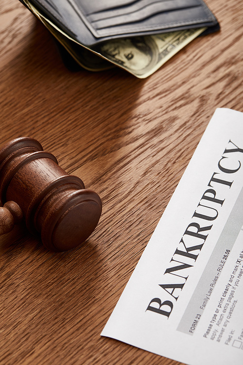 bankruptcy form with wooden gavel, dollar banknote in wallet on brown wooden table