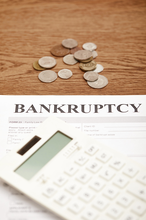 selective focus of bankruptcy form, calculator and coins on brown wooden table