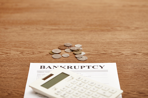 selective focus of bankruptcy form, calculator and coins on brown wooden table with copy space