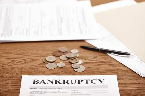 selective focus of bankruptcy form, coins and documents on brown wooden table