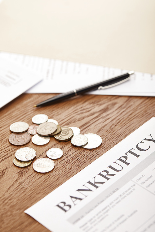 selective focus of bankruptcy form, pen, coins and documents on brown wooden table