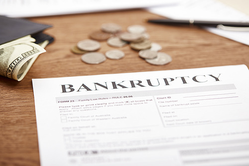 selective focus of bankruptcy form, wallet with dollar banknote, coins and documents on brown wooden table