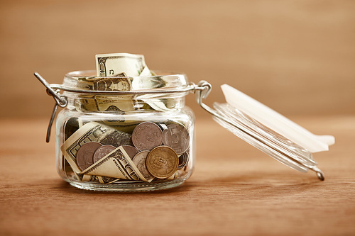 glass jar with coins and dollar banknotes on wooden table