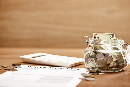 selective focus of bankruptcy form, coins, calculator and glass jar with dollar banknotes