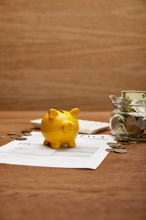 selective focus of bankruptcy form, coins, yellow piggy bank, calculator and glass jar with dollar banknotes on wooden table