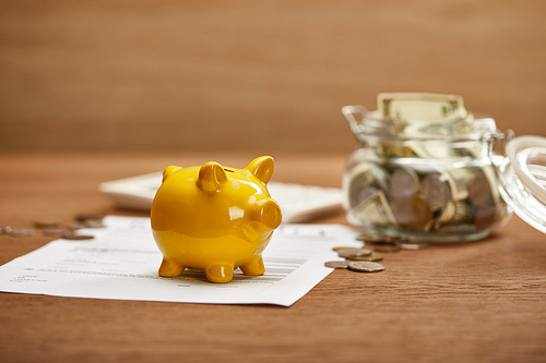 selective focus of bankruptcy form, coins, yellow piggy bank and glass jar with dollar banknotes on wooden table