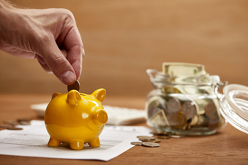 cropped view of man putting coin in yellow piggy bank