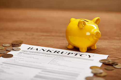 selective focus of bankruptcy form, coins, yellow piggy bank on wooden table