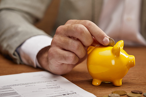 close up view of businessman putting coin in yellow piggy bank at wooden table