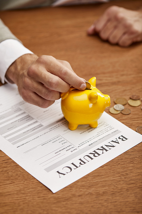 cropped view of man putting coin in yellow piggy bank on bankruptcy form