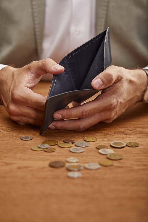 cropped view of man showing empty wallet near coins on wooden table