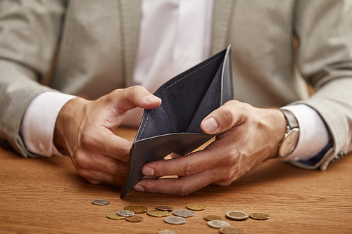 partial view of man showing empty wallet near coins on wooden table