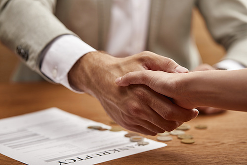 cropped view of businessman and businesswoman shaking hands at wooden table