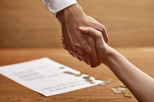 selective focus of man and woman shaking hands near bankruptcy form and coins