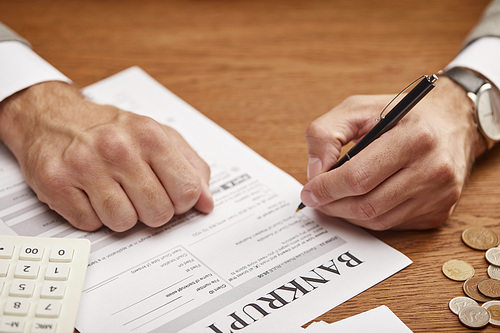 cropped view of man filling in bankruptcy form at wooden table