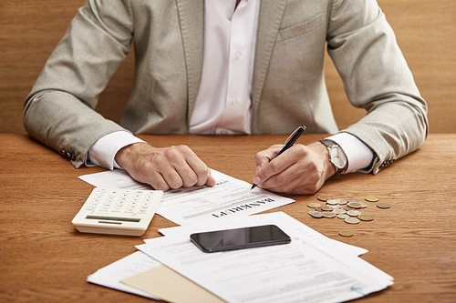 cropped view of businessman in suit filling in bankruptcy form at wooden table