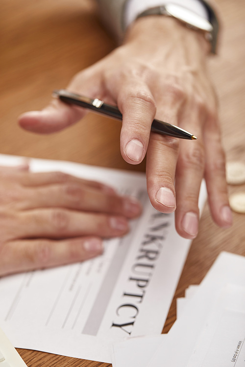 cropped view of businessman holding pen above bankruptcy form at wooden table