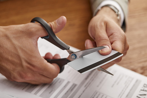 partial view of businessman cutting credit card with scissors at wooden table