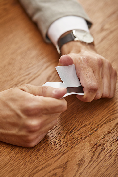 partial view of businessman breaking credit card at wooden table