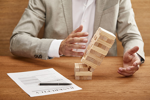 partial view of businessman in suit breaking tower made of wooden blocks near bankruptcy form