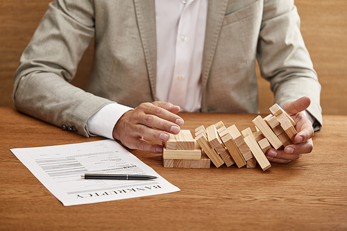 partial view of businessman in suit holding fallen tower made of wooden blocks near bankruptcy form