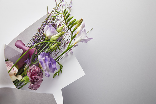 top view of violet bouquet wrapped in paper on white background