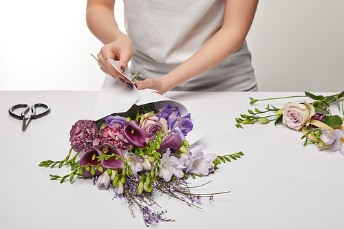 cropped view of florist wrapping violet bouquet in paper isolated on white