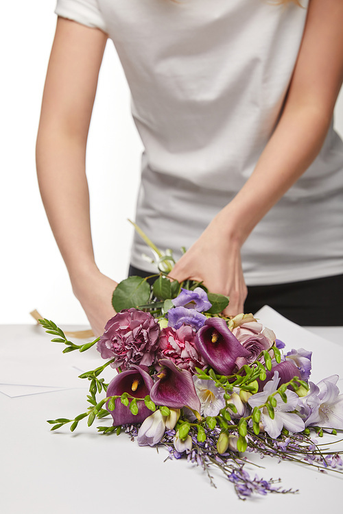 cropped view of florist wrapping violet bouquet in paper isolated on white