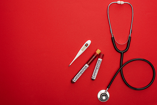 Top view of stethoscope, thermometer and test tubes with blood samples and coronavirus lettering on red background