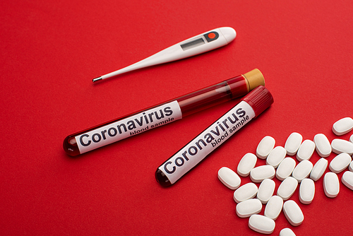Pills, thermometer and test tubes with blood samples and coronavirus lettering on red surface