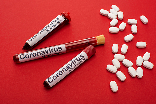 Close up view of pills and test tubes with blood samples and coronavirus lettering on red background