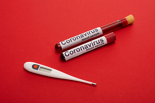 Close up view of thermometer, test tubes with blood samples and coronavirus lettering on red background