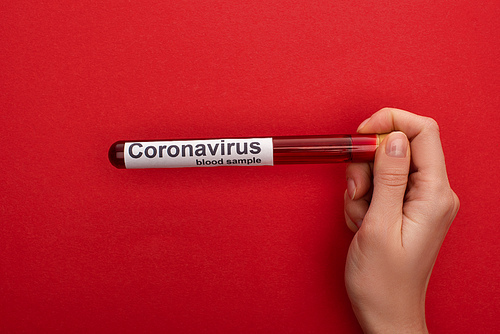 Top view of woman holding test tube with blood sample and coronavirus lettering on red background