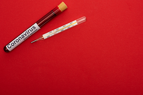 Top view of test tube with blood sample and coronavirus lettering and thermometer on red background