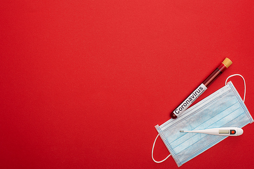 Top view of test tube with blood sample and coronavirus lettering, medical mask and thermometer on red background