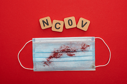 Top view of medical mask with blood and ncov letters on wooden blocks on red background