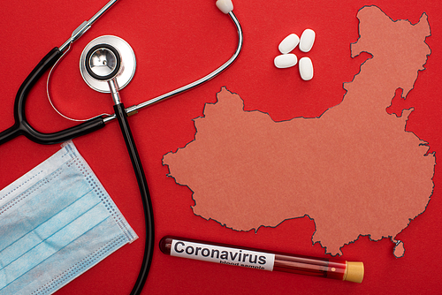Top view of stethoscope, medical mask and test tube with coronavirus lettering near map of china on red background
