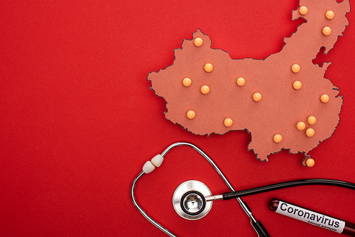 Top view of push pins on map of china with stethoscope and test tube with coronavirus lettering on red background