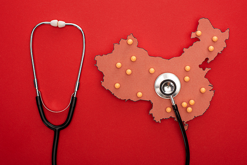 Top view of map of china with push pins and stethoscope on red background