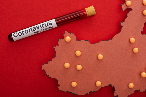 Top view of map of china with push pins and test tube with blood sample and coronavirus lettering on red background