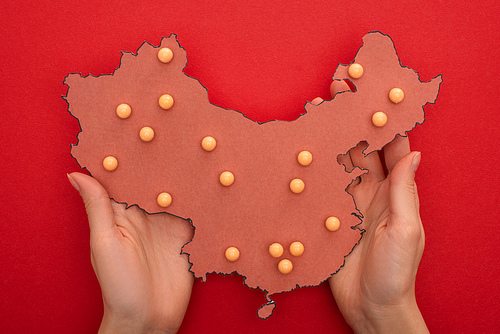 Top view of woman holding layout of china map with push pins on red background