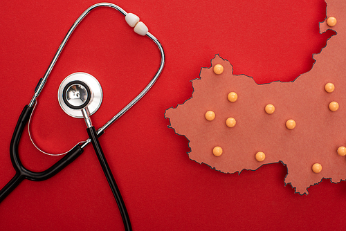 Top view of stethoscope and layout of china map with push pins on red background