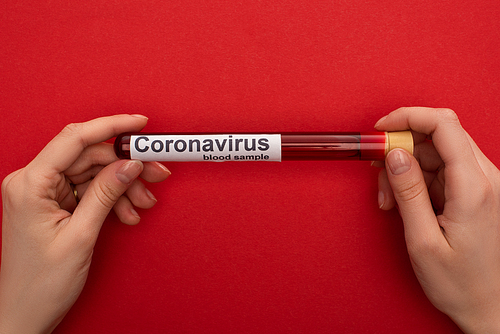 Top view of woman holding test tube with blood sample and coronavirus lettering on red surface
