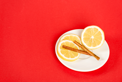 sliced lemons on saucer with cinnamon sticks on red