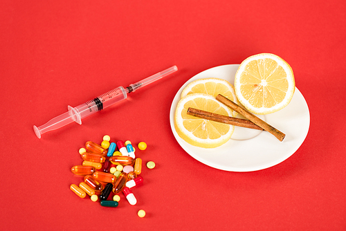 syringe near sliced lemons, cinnamon sticks and pills on red