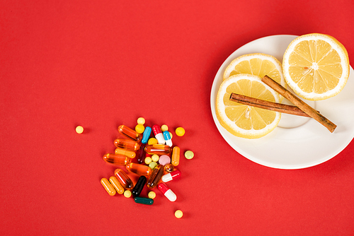 top view of sliced lemons and cinnamon sticks near pills on red