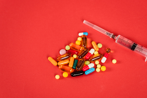 top view of colorful pills near syringe on red with copy space