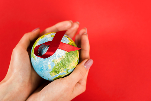 cropped view of woman holding globe with red ribbon as hiv awareness isolated on red