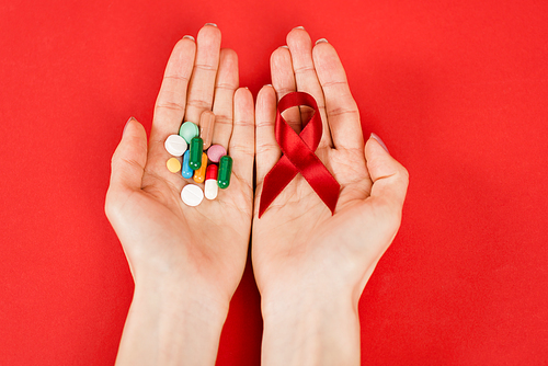 top view of woman holding red ribbon as hiv awareness and pills on red