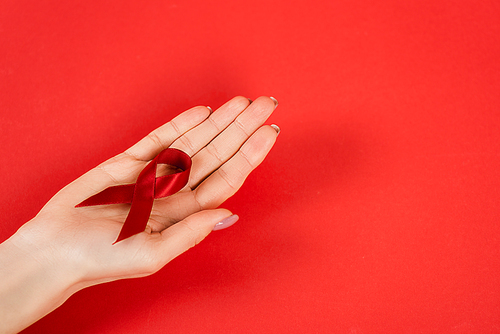 cropped view of woman holding red ribbon as hiv awareness on red